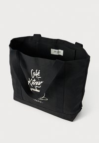 Svart lerret tote-veske med robuste håndtak, som har et trykt kaffekoppgrafikk og "Café Kitsuné - Paris" tekst foran.
