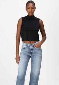 Top corto senza maniche di colore nero con collo alto, abbinato a jeans a gamba dritta di un leggero blu con una texture di denim sbiadito e design a cinque tasche.