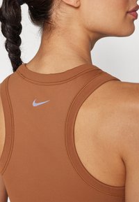 Smeđa atletska majica bez rukava s okruglim izrezom i uskim naramenicama. Na leđima se nalazi mali svijetloplavi Nikeov znak.