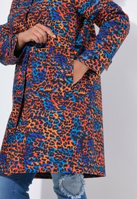 Kleurvolle luipaardprintjas met oranje, blauwe en zwarte patronen. De jas heeft zakken en een ontspannen pasvorm met lange mouwen.