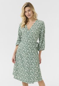 Rochie verde cu un model floral cu flori albe, cu mâneci trei sferturi, decolteu în V și o curea la talie.