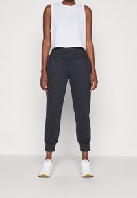 Black jogger pants with elasticized waistband and cuffs, paired with a white sleeveless crop top. Featuring a smooth fabric texture.