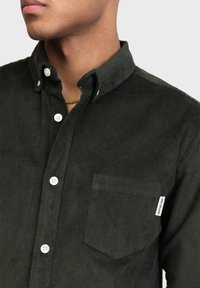 Donkergroene corduroy overhemden met een button-down kraag, witte knopen, een borstzak en een label aan de zijkant. Zachte textuur.