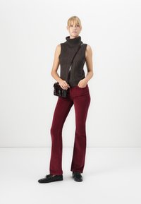 Haut sans manches en laine sombre avec un col haut, associé à un pantalon en velours côtelé bordeaux évasé et un petit sac à bandoulière noir. Chaussures noires.
