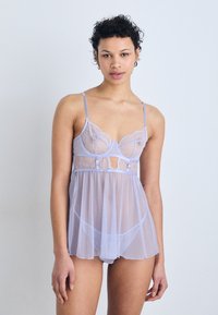 Babydoll transparent lila cu accente din dantelă, croială stil pijama, bretele ajustabile și textură cu buline. Prezentă un design cu decupaj la mijloc.