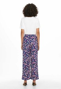 Kwiatowe spodnie o szerokich nogawkach z granatowym tłem i różowymi oraz fioletowymi wzorami kwiatów, zestawione z krótką białą bluzką.