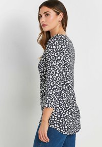 Top con stampa leopardata in bianco e nero, con maniche a tre quarti, scollatura rotonda e parte posteriore leggermente più lunga. Tessuto morbido e vestibilità comoda.