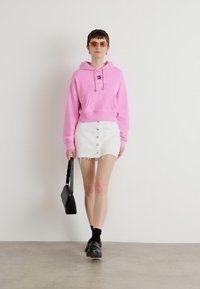 Felpa rosa chiaro con grafica a stella, abbinata a una gonna di jeans bianca con bottoni frontali e orlo sfilacciato, accessoriata con una borsa nera.