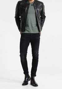 Sort læderjakke med ribbede skuldre, grøn skjorte, sort slim-fit jeans og sorte ankelstøvler. Glat tekstur og tætsiddende design.