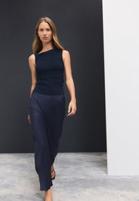 Camiseta sin mangas azul marino con un escote asimétrico combinada con una falda larga fluida azul marino. Textura suave y diseño minimalista sin patrones visibles.