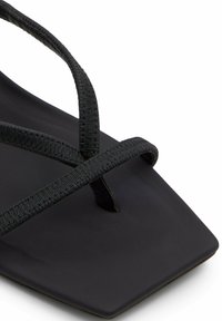 Black flat sandal featuring a square toe, thin woven straps, and a smooth matte footbed. Minimalist design with a sleek profile.