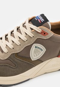 Brune daim og mesh sneakers med en triangel logo-patch, kremfargede snørebånd og diskrete røde detaljer. Har en tykk teksturert såle.