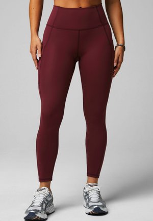 Maroon high-waisted leggings with a smooth texture and contrasting seams, paired with silver athletic shoes featuring a mesh design.