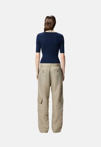 Top corto a righe in colore blu navy abbinato a pantaloni cargo beige con tasche laterali e una vestibilità comoda, cuciture visibili e una texture liscia.