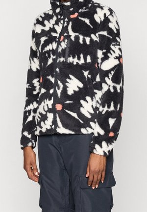 Czarna polarowa kurtka z białymi i koralowymi abstrakcyjnymi wzorami, z suwakiem z przodu, kieszenią na piersi i metką "ROXY" na lewym rękawie, noszona z ciemnymi spodniami.