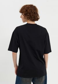 Black oversized t-shirt with short sleeves and a crew neck. Smooth cotton fabric, minimal design, no visible patterns or logos.