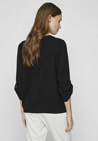 Svart blus med trekvartsärmar, mjuk textur, rundad nederkant och uppvikt ärm. I kombination med ljusa byxor.