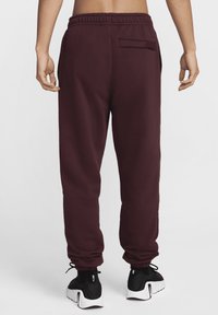 Burgundy sweatpants med elastisk midja, smalnande muddar och en bakficka. I kombination med svarta träningsskor med vita sulor.