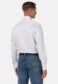 Weiße und blaue gestreifte Hemdbluse mit langen Ärmeln, Knopfmanschetten und Stehkragen, kombiniert mit blauen Jeans, die einen lässigen Stil zur Schau stellt.