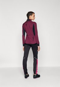 Bærrøde zip-up jakke med sorte accenter, elastisk talje og sidelommer, parret med sorte bukser med pink striber og reflekterende detaljer.
