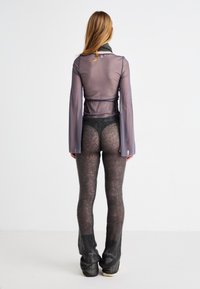 Gjennomsiktig langermet topp i grått med en innsvinget midje, kombinert med teksturerte svarte leggings med et åpen-strikket mønster og en utvidet design.