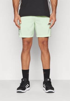 Hellgrüne Sportshorts mit normaler Passform. Mit einem adidas-Logo auf der linken Seite. Kombiniert mit schwarzen Socken und Turnschuhen.
