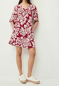Robe florale rouge avec motifs blancs, décolleté en V, manches courtes et poches. Assortie à des baskets blanches à plateforme. Tissu doux, coupe décontractée.