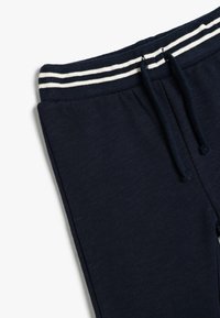 Marineblaue Jogginghosen aus strukturiertem Stoff, mit einem gerippten Bündchen mit weißen Streifen und einem Kordelzug zur Anpassung.