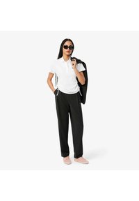 Maglietta polo bianca con colletto e cordini laterali, abbinata a pantaloni larghi a quadri neri e sneakers rosa chiaro. Inclusi occhiali da sole neri.