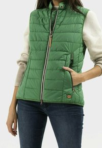 Gilet matelassé vert avec col montant, devant zippé et poches latérales. Présente un tricot beige texturé sur les épaules et un accent de logo.