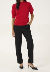 Czerwony sweter z krótkim rękawem, pleciony w prążki, z kołnierzem typu mock; w połączeniu z czarnymi, luźnymi spodniami; czarne klapki na obcasie z dekoracyjnym detalem.