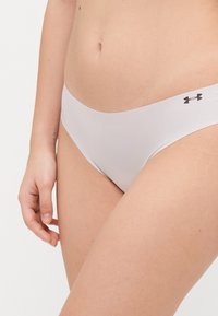 Pilka, tampri apatinė trikotažas su mažo juosmens kirpimu ir elastinga juosta, ant šono esantis mažas juodas logotipas. Lygi tekstūra.