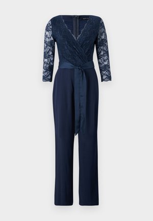 Marineblå jumpsuit med lange blonderærmer, dyb V-udskæring og omslag design. Udstyret med et satinbælte og lige benbukser. Teksturerede blonde detaljer.