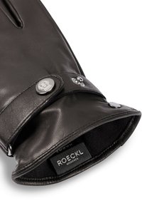 Schwarze Lederhandschuhe mit weichem Innenfutter, ausgestattet mit einem umgeschlagenen Bund, der mit zwei Druckknöpfen befestigt ist, und einem Etikett mit der Aufschrift "ROECKL MÜNCHEN."