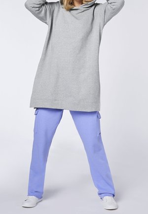 Felpa con cappuccio di un grigio chiaro con vestibilità comoda, abbinata a pantaloni cargo di colore lavanda dotati di tasche laterali e una texture liscia. Scarpe da ginnastica bianche completano il look.