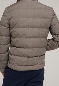 Chaqueta acolchada gris con un patrón de cuadros, tejido con textura y acolchado horizontal. Cuenta con un cuello alto y una silueta ajustada en la cintura.