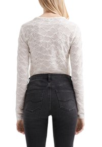 Langarmshirt in off-white met een gestructureerd geometrisch patroon. Gecombineerd met high-waisted zwarte jeans met achterzakken en stiksel details.