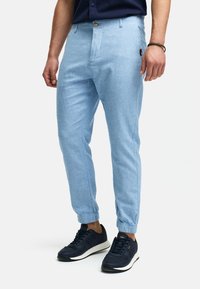 Pantalones tapered de color azul claro, confeccionados en una tela suave con puños elásticos, bolsillos frontales y un cierre de botón en la cintura. Llevados con zapatillas negras.