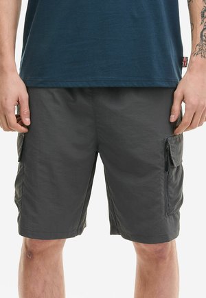 Muškarac odjeven u tamnosive cargo kratke hlače s džepovima na patentni zatvarač i preklop te tamnoplavu košulju, pokazujući tetovaže na lijevoj podlaktici.