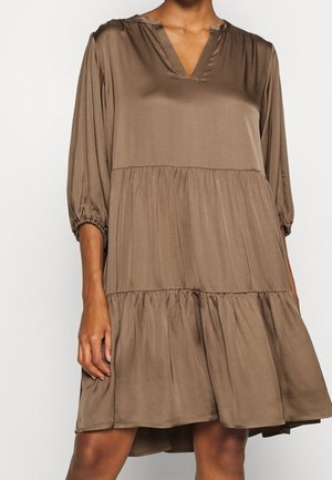 Locker sitzendes braunes Kleid mit gestuftem Rock, dreiviertelärmeln mit elastischen Bündchen und V-Ausschnitt an einer Person.