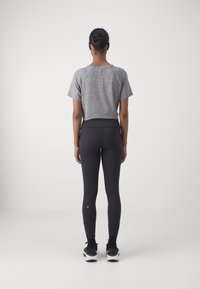 Šedé zkrácené tričko s krátkými rukávy a zaobleným lemem, doplněné o vysoké černé legíny. Černé tenisky outfit dokončují.
