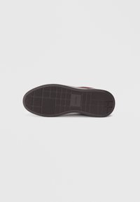 Suela de zapato de goma marrón con patrones de agarre texturizados y un logotipo elevado. Diseño de borde suave con forma contorneada para mayor comodidad.
