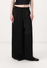 Black wide-leg trousers with an elastic waistband, featuring a smooth texture and a tailored fit, paired with a black cropped top.