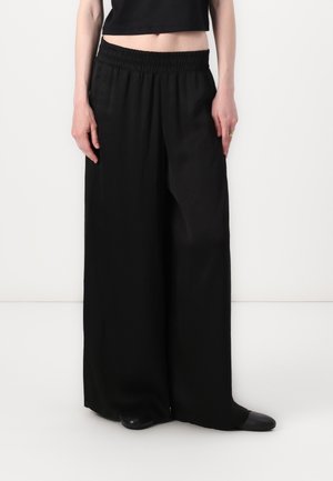 Black wide-leg trousers with an elastic waistband, featuring a smooth texture and a tailored fit, paired with a black cropped top.
