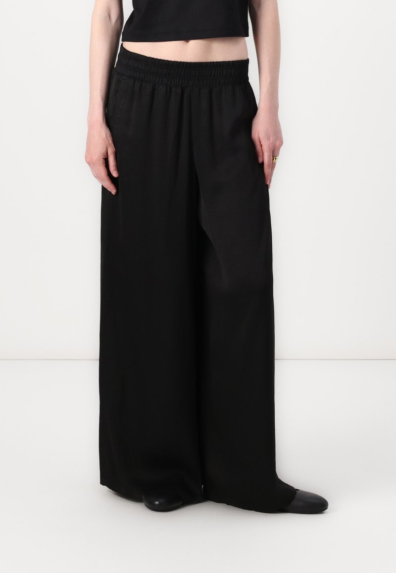Black wide-leg trousers with an elastic waistband, featuring a smooth texture and a tailored fit, paired with a black cropped top.