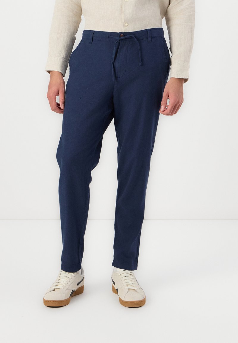Marinblå, lätta byxor med dragsko i midjan, sidofickor och smal passform. Företrädesvis med vita sneakers och en beige skjorta med knappar.
