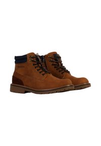Botas de ante marrón hasta el tobillo con cuello azul marino, suela de goma marrón, paneles laterales en contraste y ojales metálicos para los cordones. Marca grabada en el lateral.