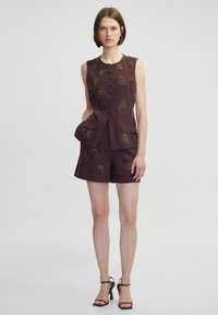 Bruin mouwloos vest en short set met geborduurde bladeraandoeningen, voorzien van een voorkant met knopen en twee zijzakken.