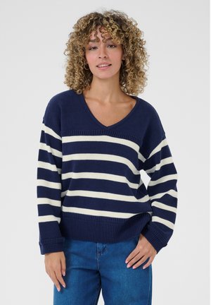 Pull rayé bleu marine et blanc avec un col en V, des épaules basses et des poignets côtelés, associé à un jean en denim bleu. Texture douce, design décontracté.