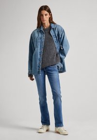 Denimhemd, grauer Strickpullover, blaue Jeans und weiße Sneakers. Merkmale sind der lockere Schnitt, Knopfleiste und dezente Abnutzungsspuren an den Jeans.